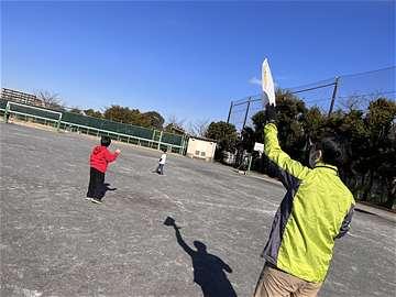 校庭でたこを掲げる大人と走り出そうとする子どもの写真