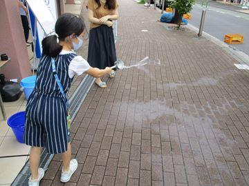 ひしゃくで歩道に水をまく人の写真
