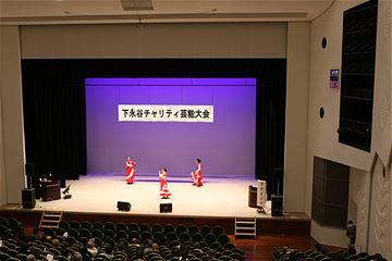 下永谷チャリティ芸能大会の横断幕が掲げられたステージの上で3人の人が踊っている写真