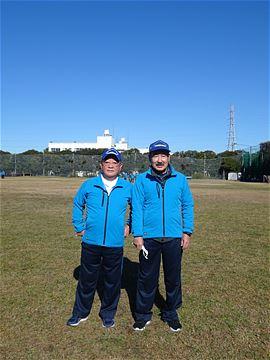 芝のグラウンドに立つ青い上着を着た2人の写真
